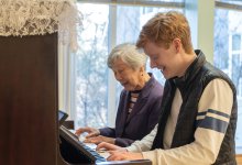 Photo of high school student and elderly woman playing piano